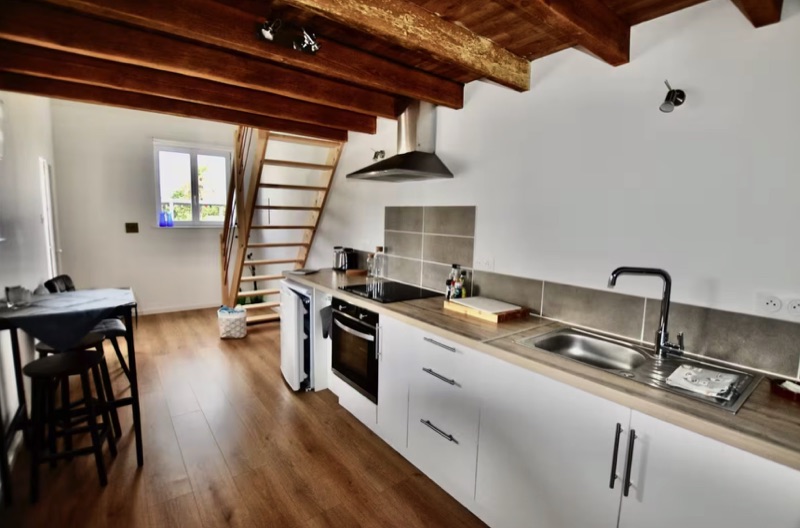 Courtyard gîte kitchen with exposed oak beams and open mezzanine staircase